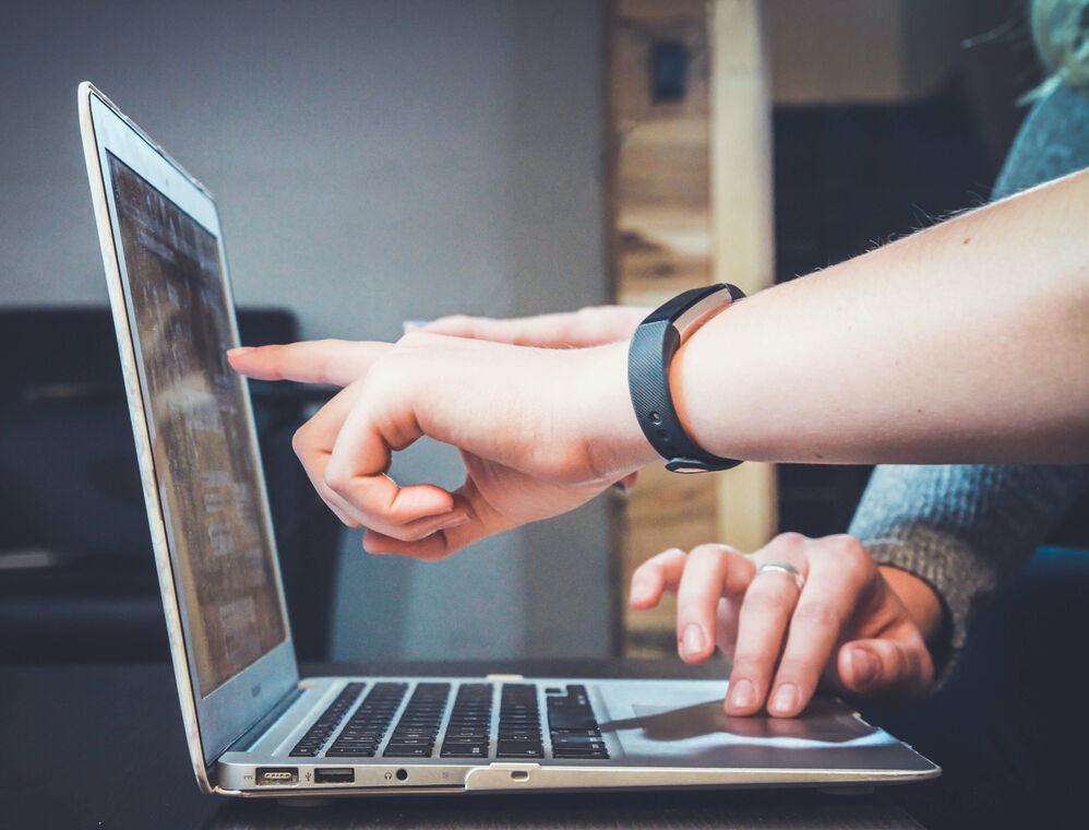 Two people sitting in front of a laptop, pointing at its screen.