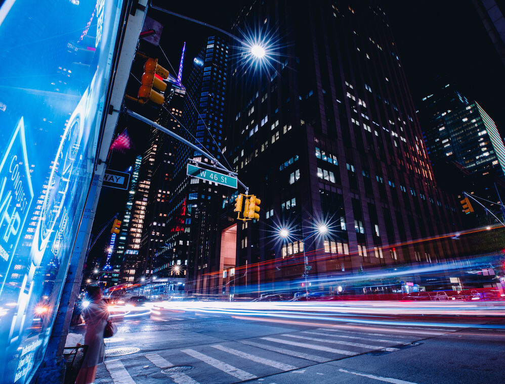 A city at night, looking up a building from the other side of the road.
