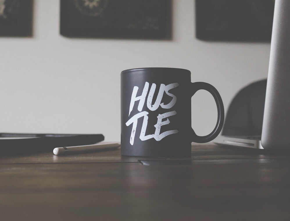 Black cup on a table with inscription "HUSTLE"