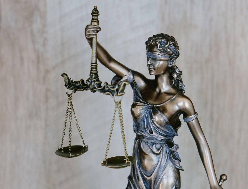 A Justitia Bronce Statue, holding the famous scale in her right hand. Her eyes are blindfolded.